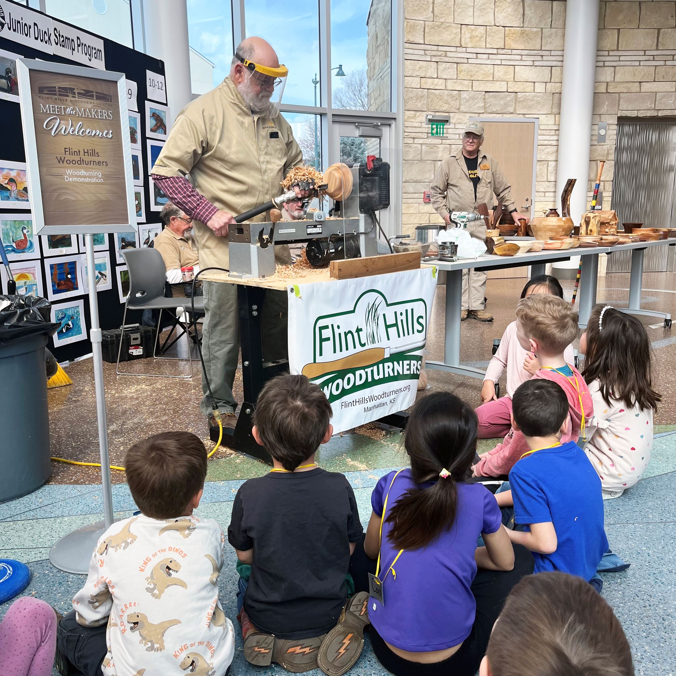 Group of young children watching a man turn wood