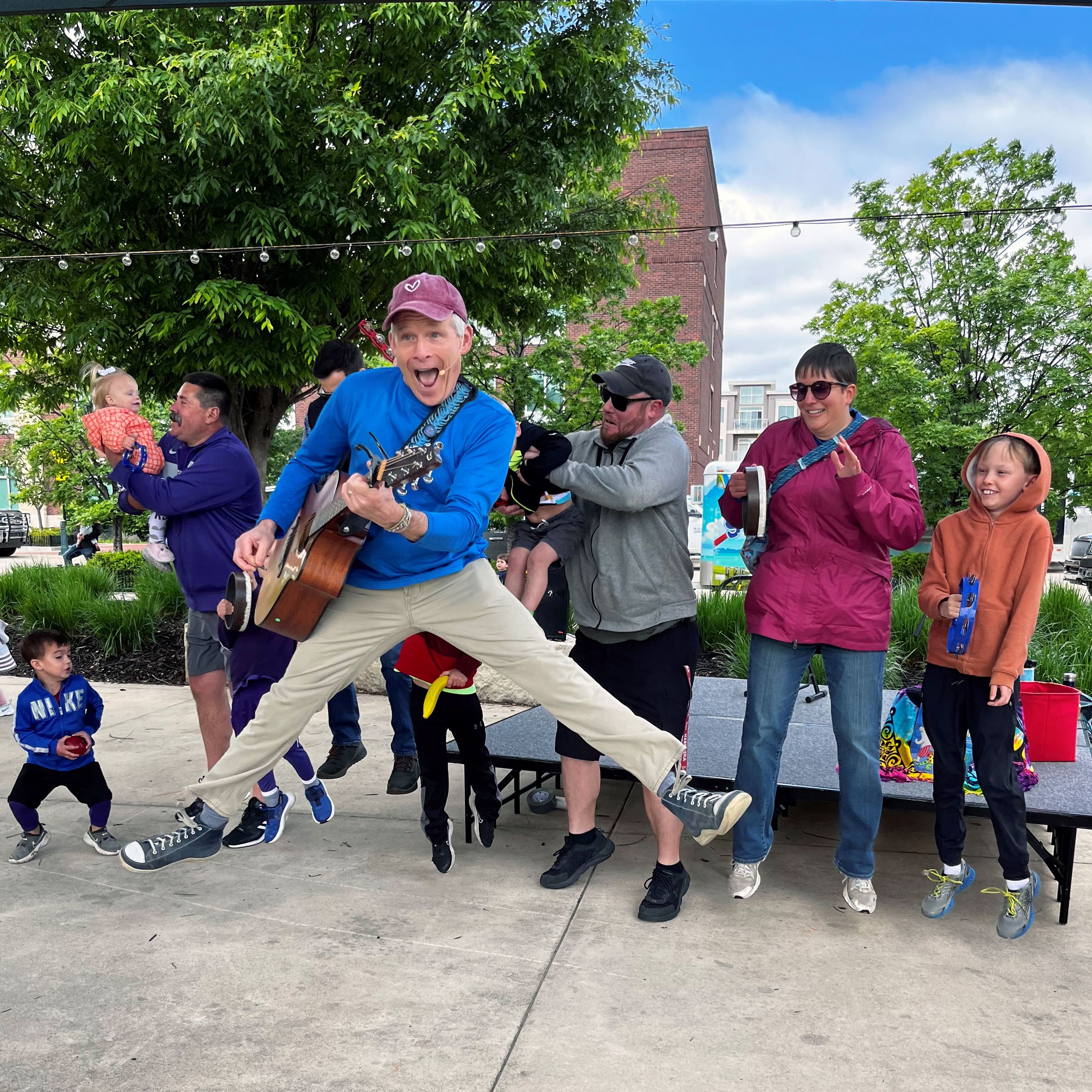 Mr. Stinky Feet playing a guitar and jumping in the air with audience participants behind him